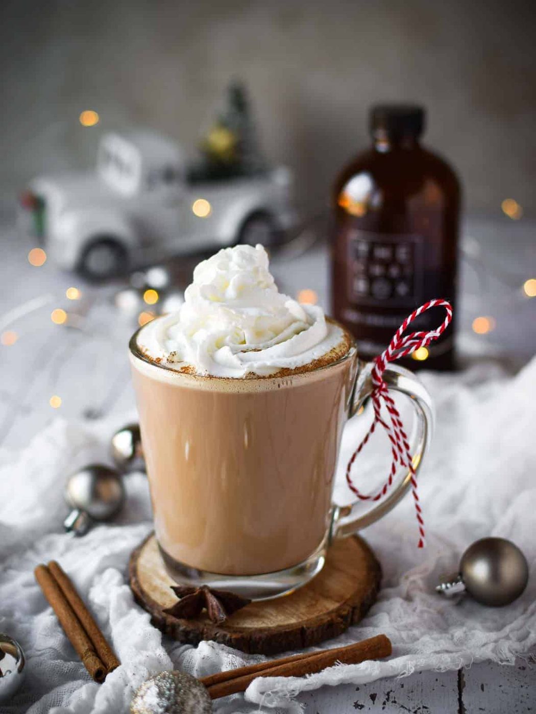 Chai eggnog latte in a clear mug with twinkle lights and ornaments around it.