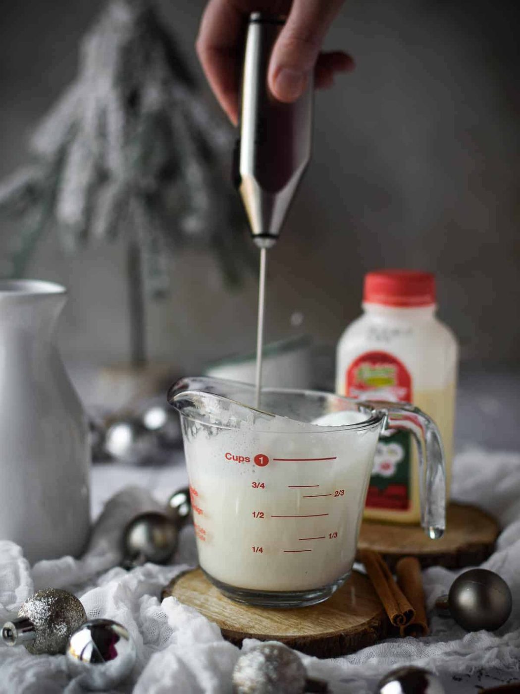 A hand shown frothing milk in a clear measuring cup.