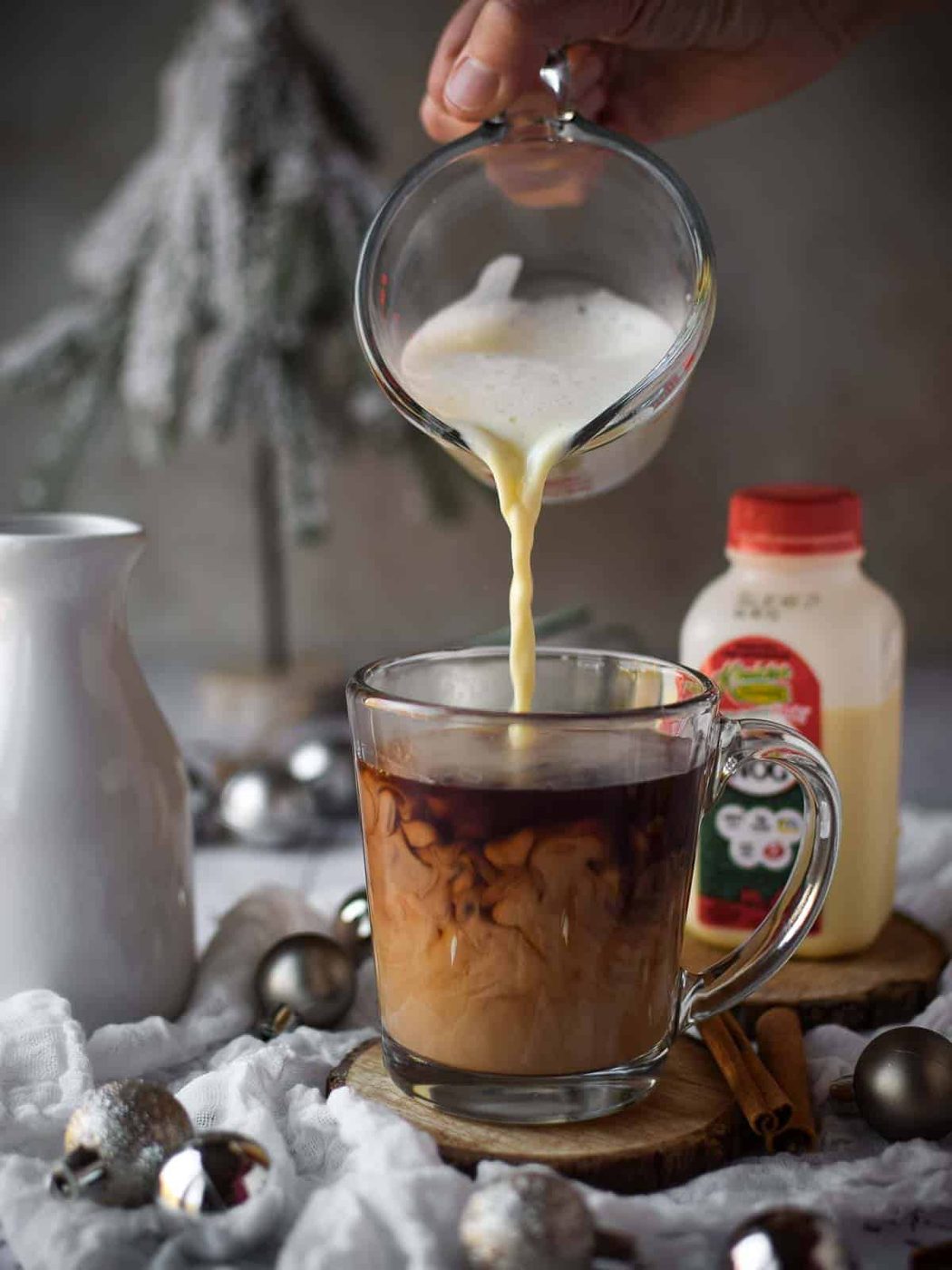 Frothed milk for a chai eggnog latte being poured into a clear mug.