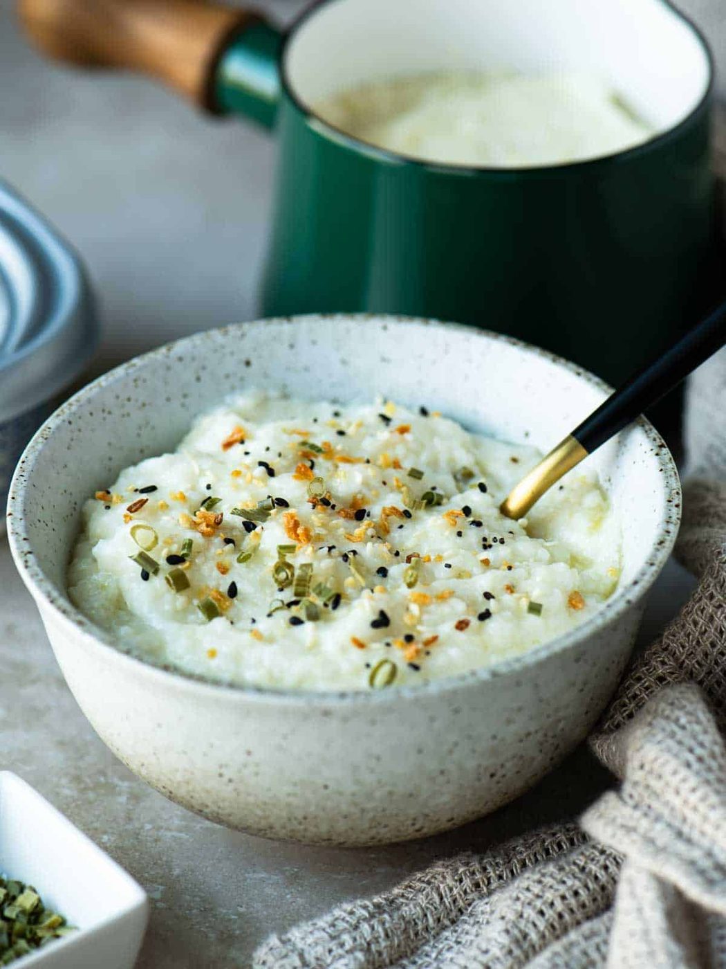 A bowl of grits with a spoon in it and a pot in the background.