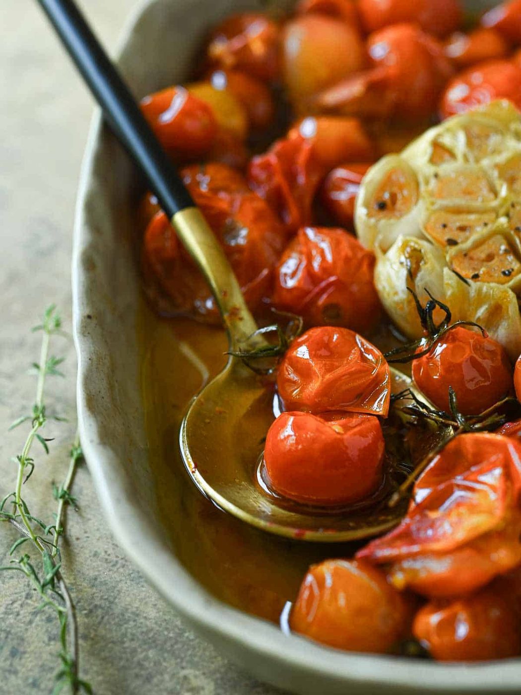 Tomato confit in a bowl with a spoon and thyme on the side.