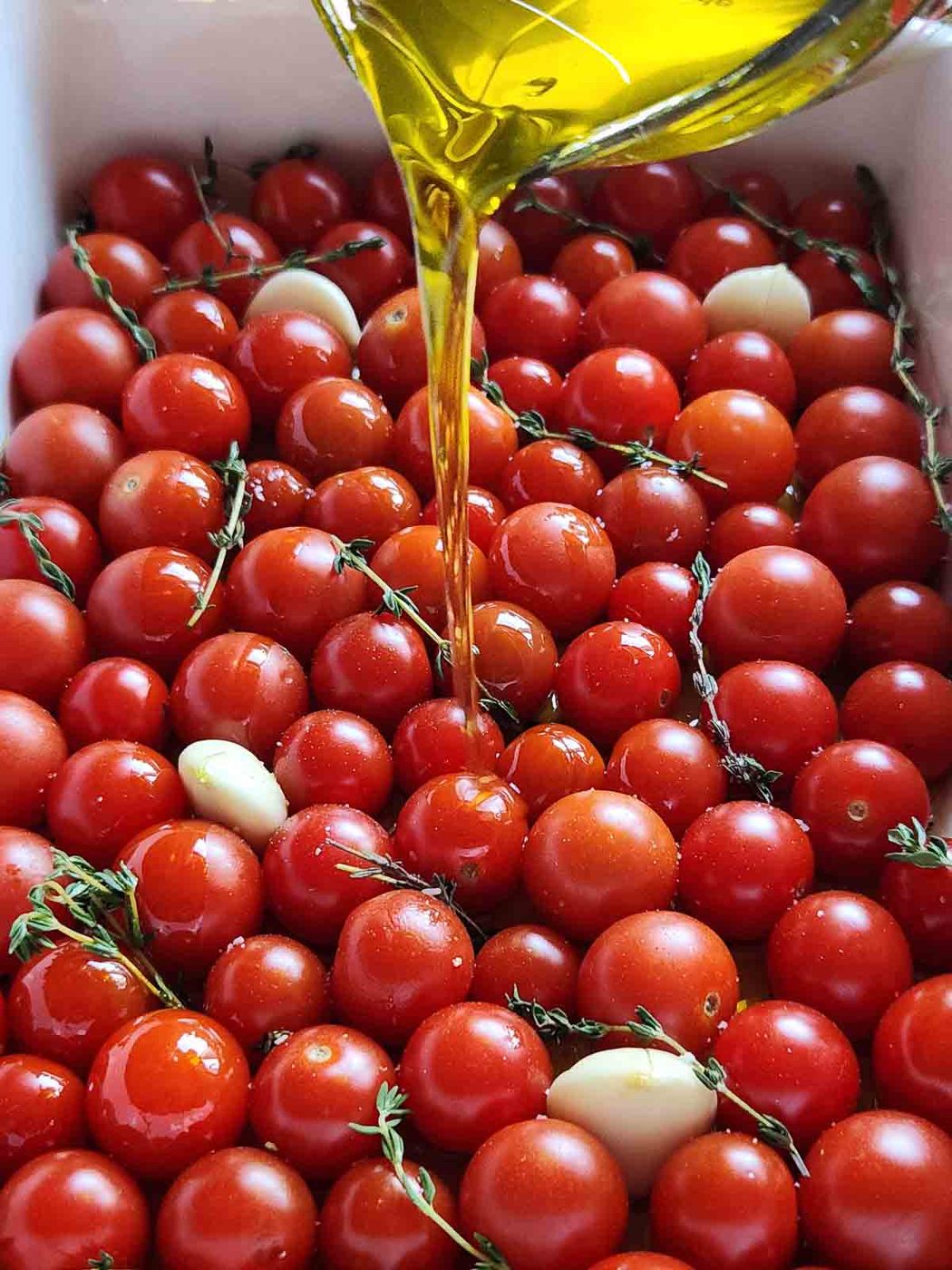 Oil being poured over tomatoes in a baking pan.