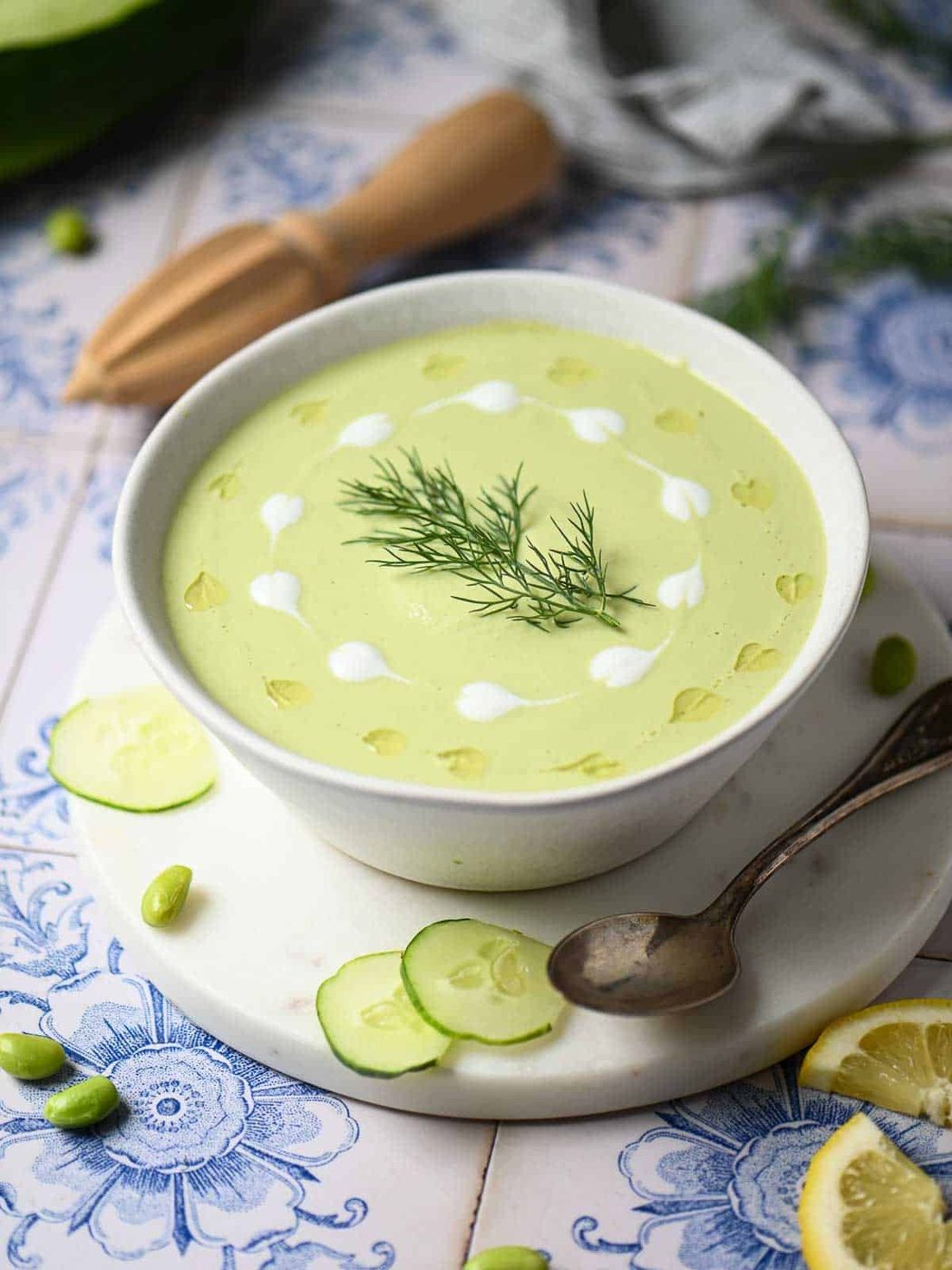Overhead of cucumber soup in a white bowl with swirls of yogurt and oil.