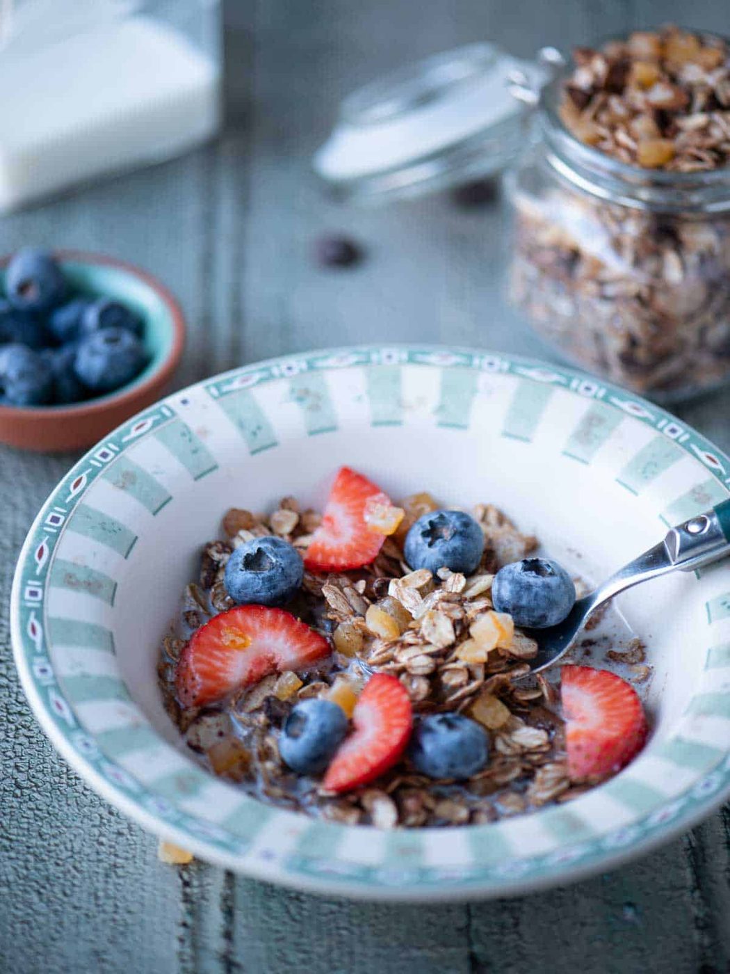 Muesli cereal in a bowl with fruit and a spoon to the right.