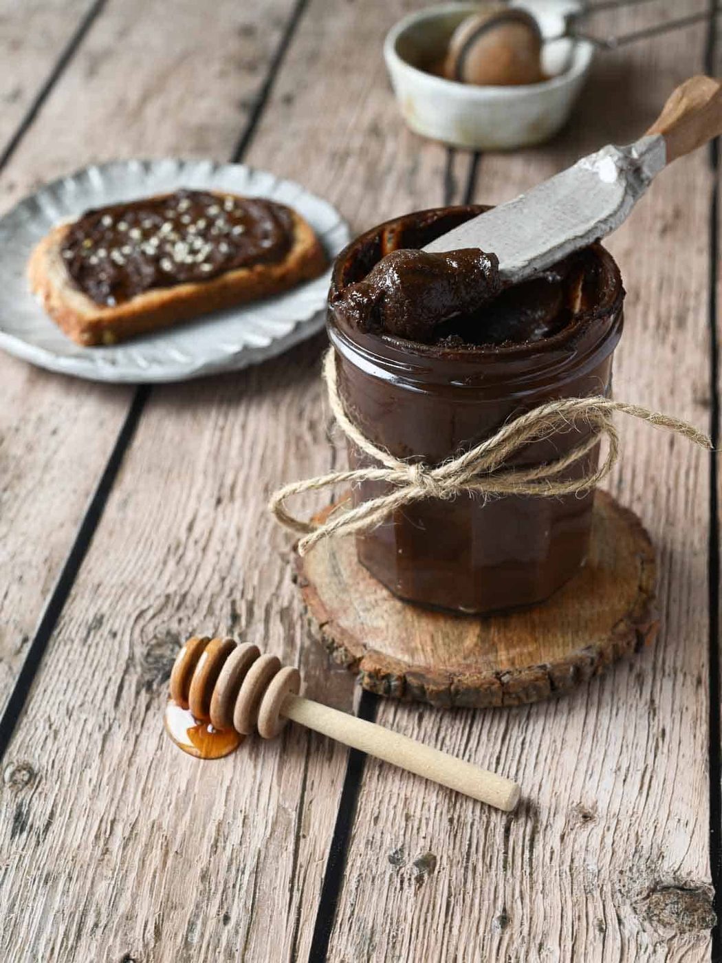 Chocolate tahini spread in a clear jay with a spreader scooping some out.