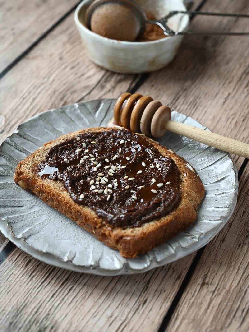 Chocolate tahini spread on toast with sesame seeds on top on top of a wood surface.
