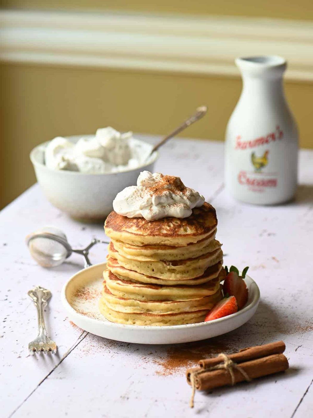 A stack of cinnamon pancakes with whipped cream on top on a white board.