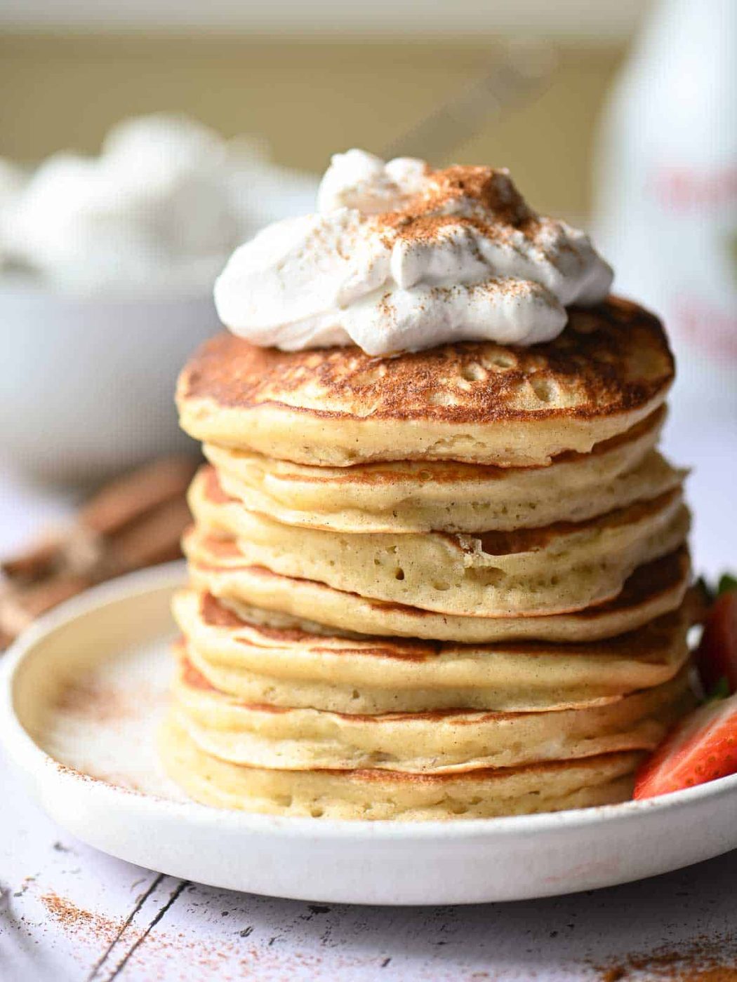 Close up of a stack of pancakes with whipped cream on top and cinnamon.