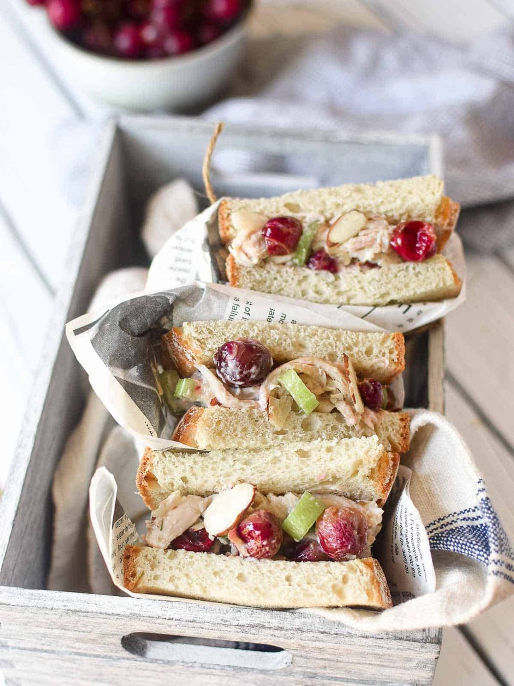 Overhead view of chicken salad with roasted grape sandwiches wrapped in deli paper placed in a grey box