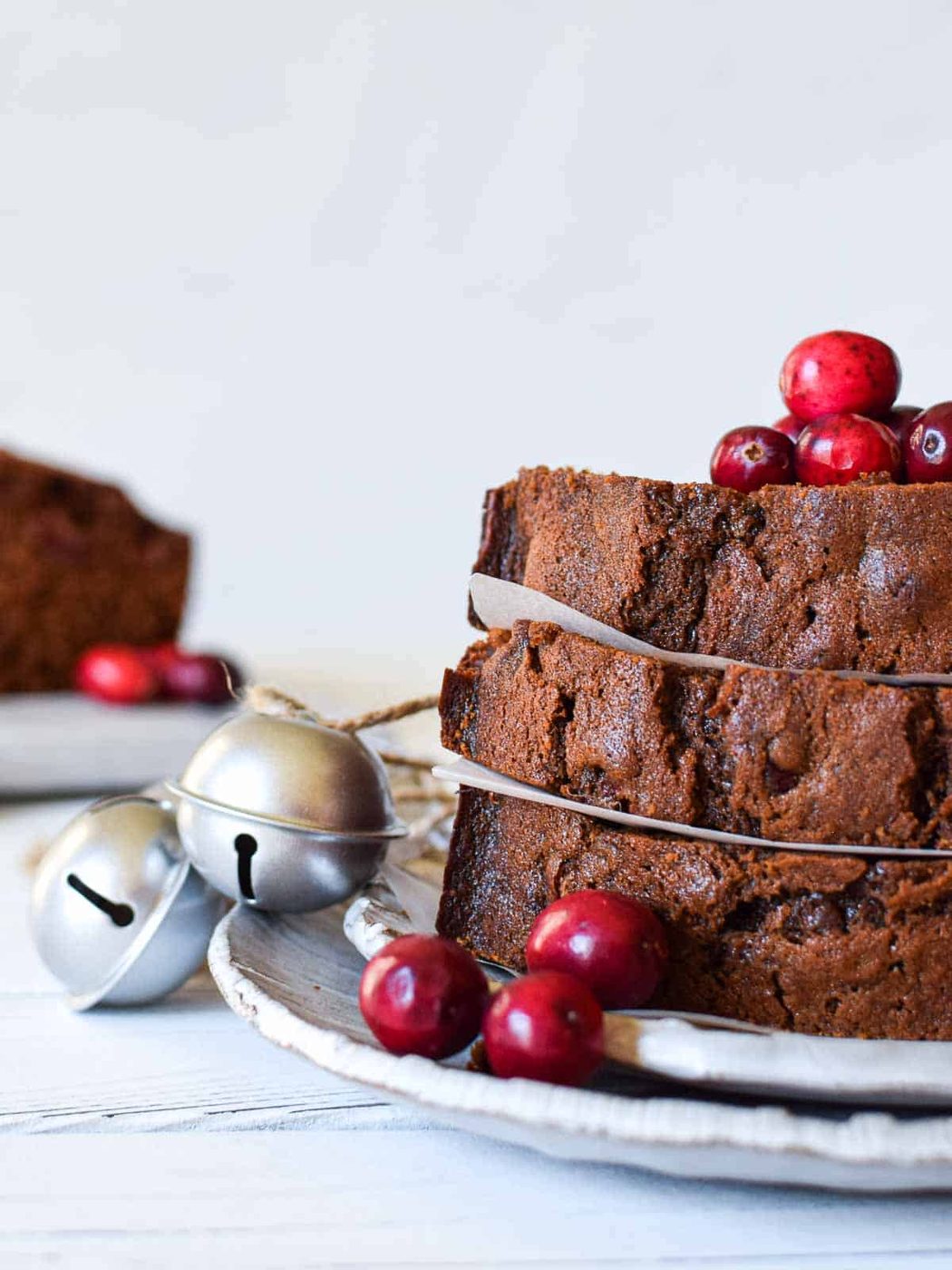 Eye-level view of slices of cranberry loaf with cranberries and bells next to it.