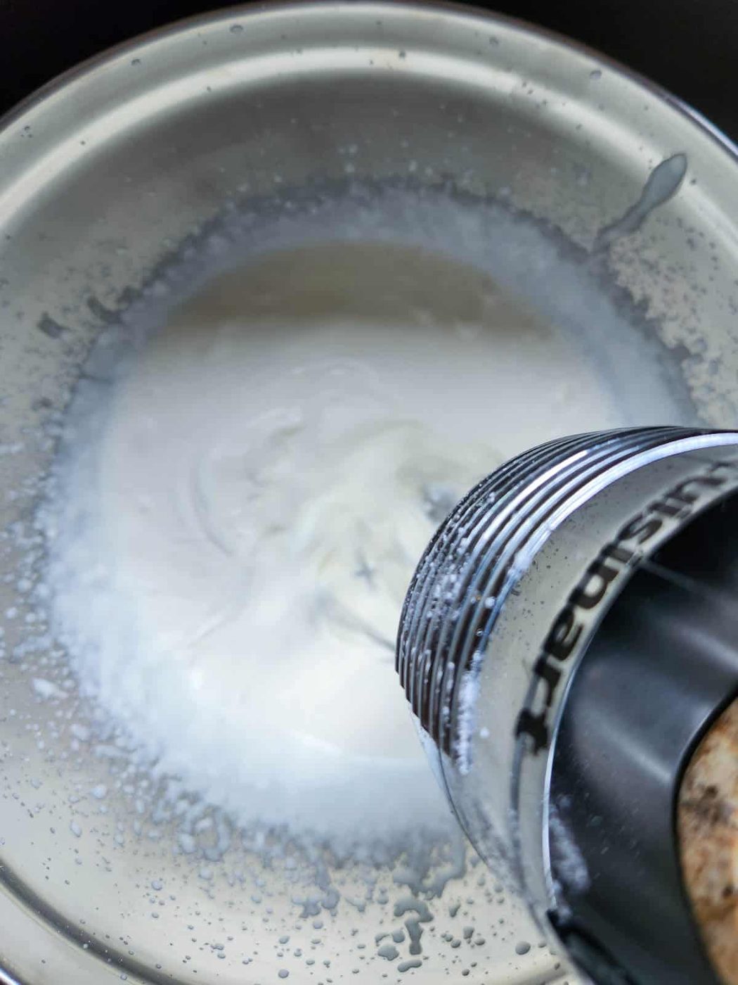 A hand mixer in a bowl with cream.