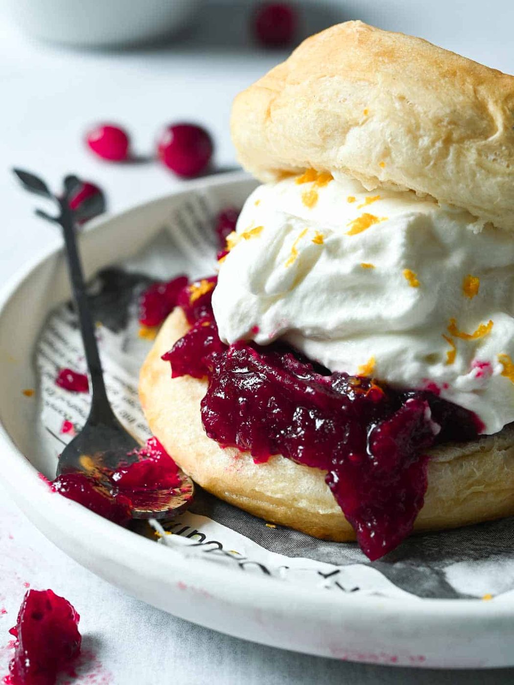 Close-up of shortcake dessert with cranberry and whipped cream on a white plate.