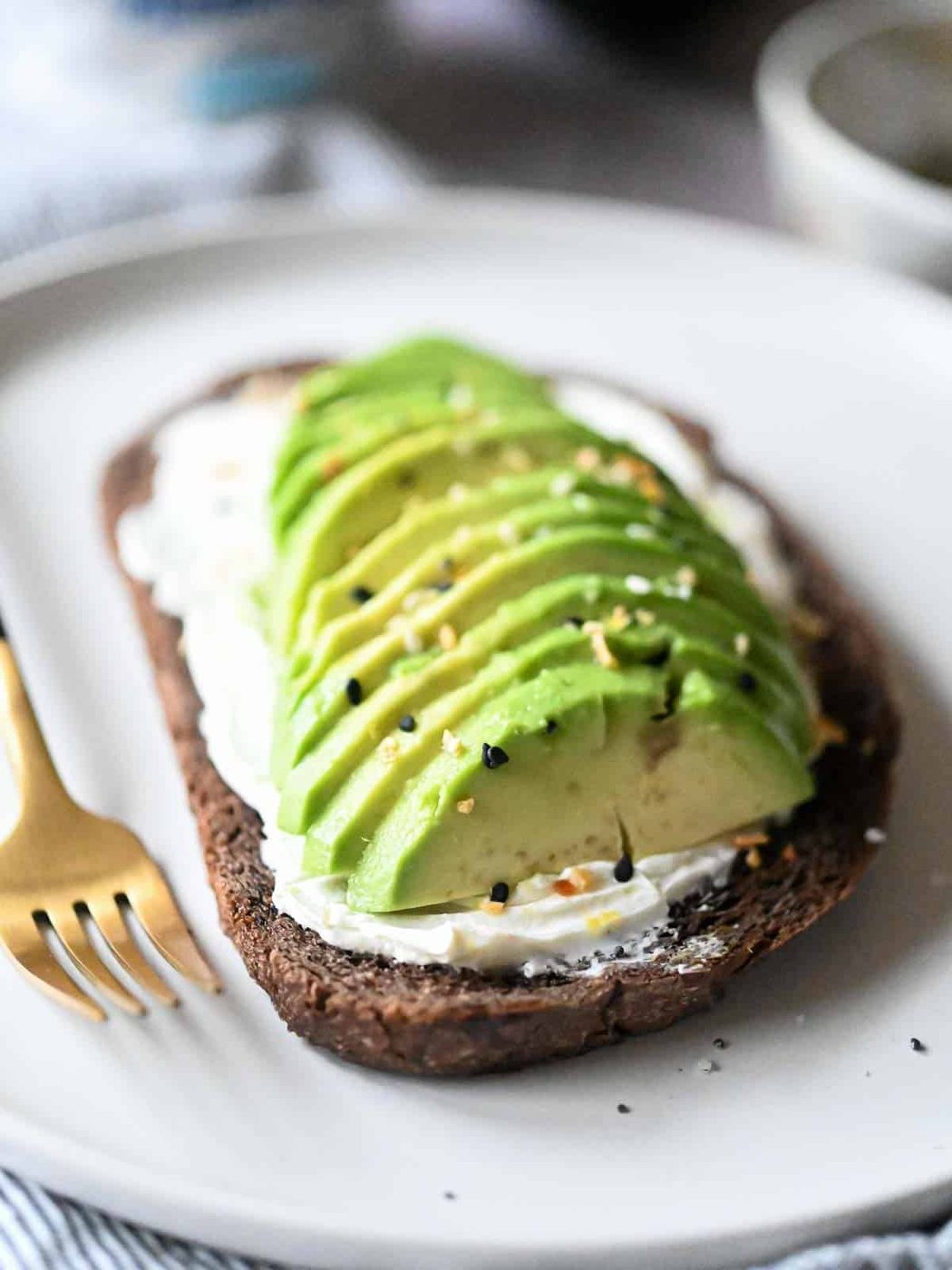 Sliced avocado on pumpernickel bread with cream cheese and spices.