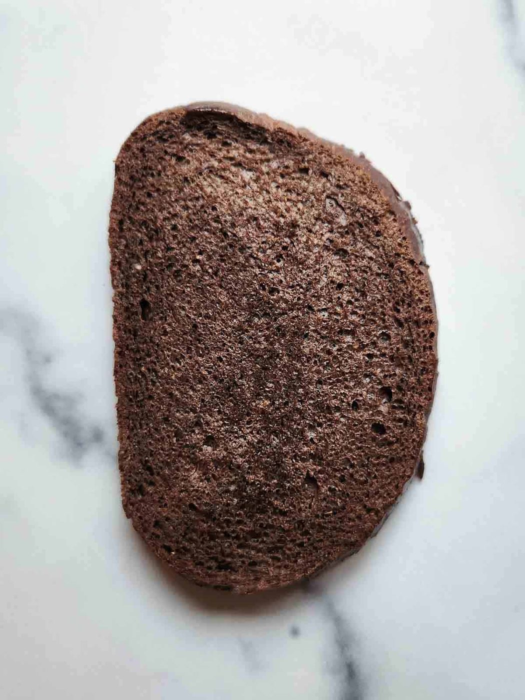 One slice of pumpernickel bread on white marble.