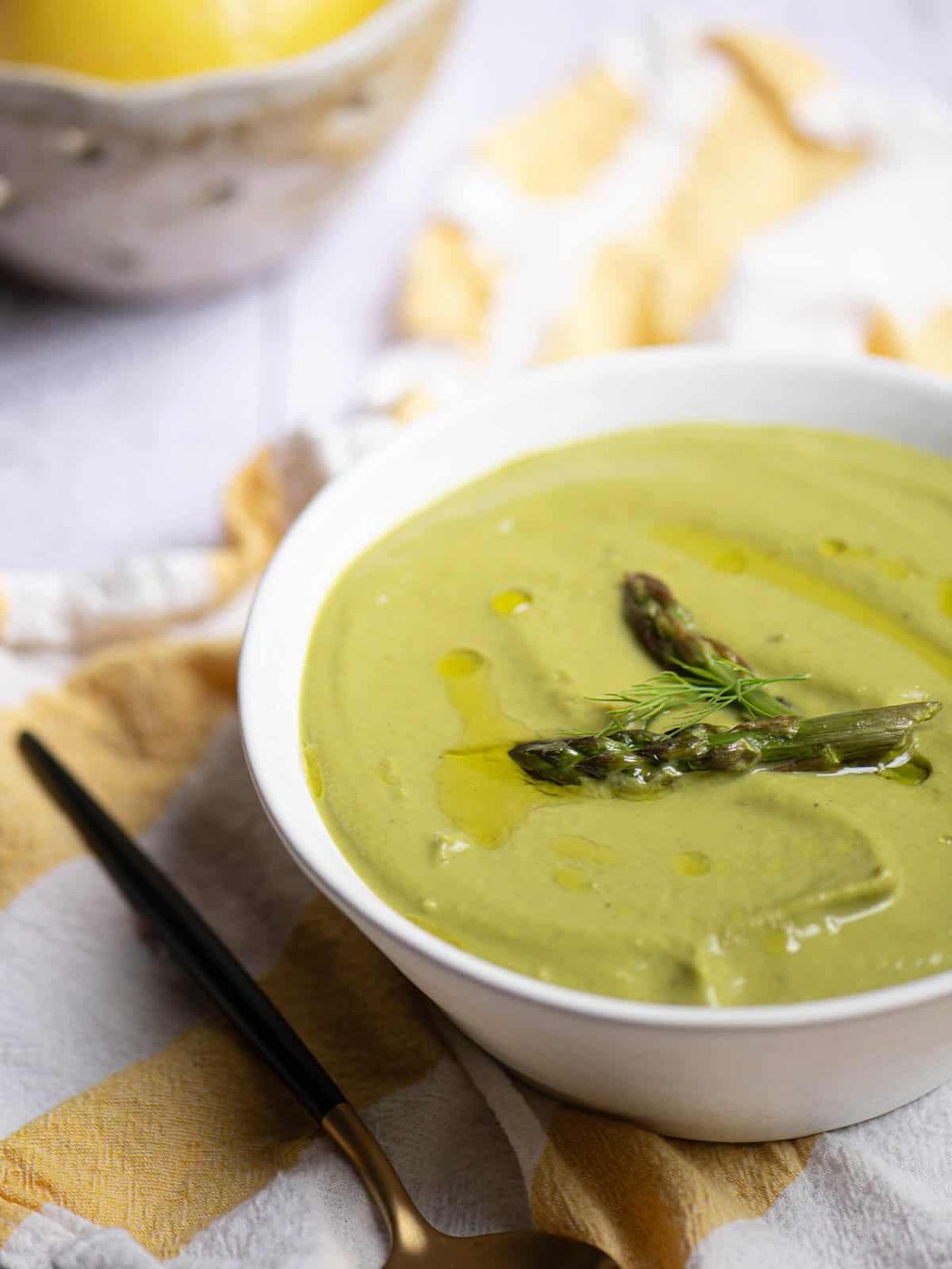 Angled view of asparagus soup in a white bowl with a lemon in the background.