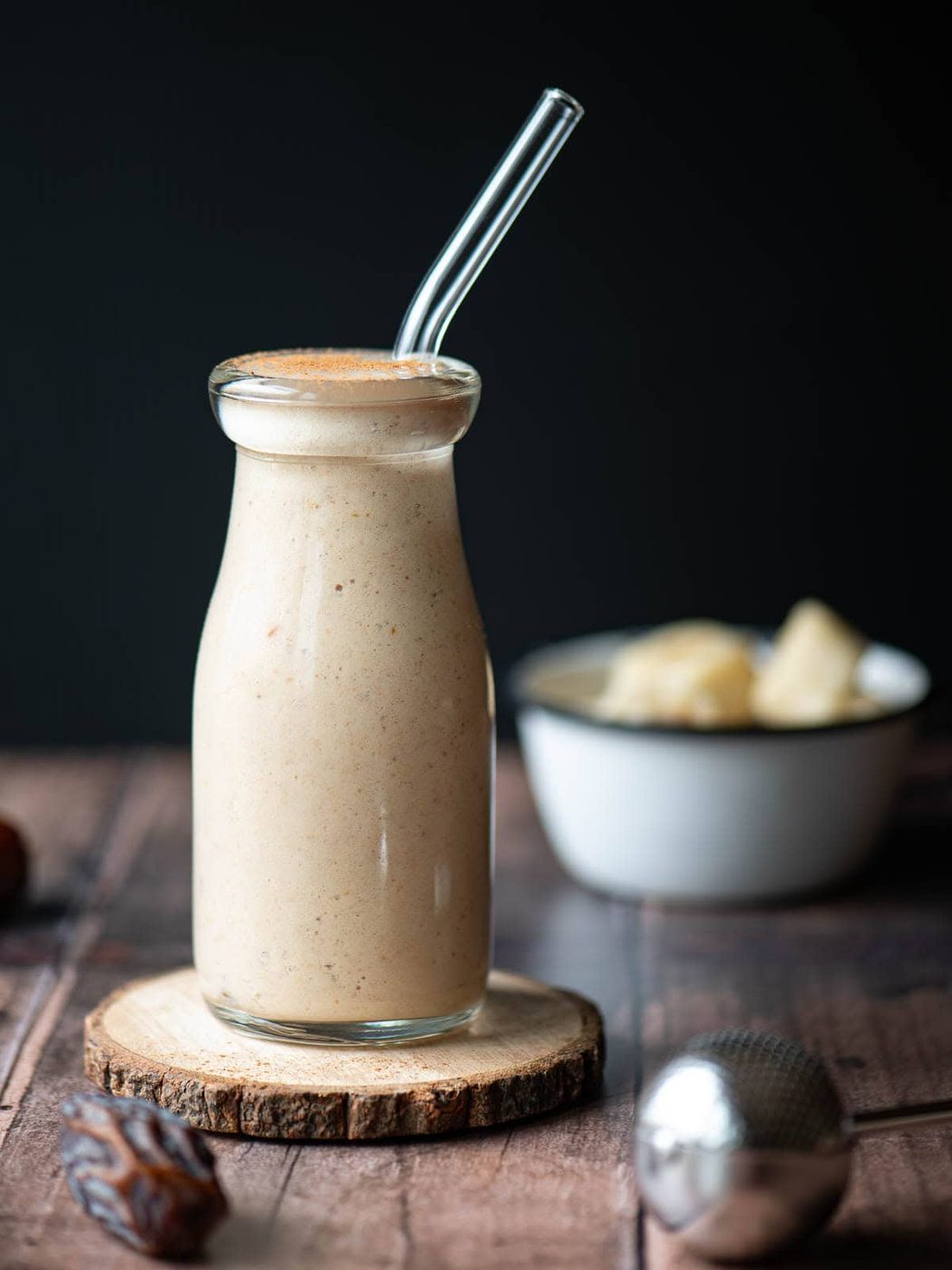 Eye level smoothie in a clear glass with a glass straw on a wood surface.