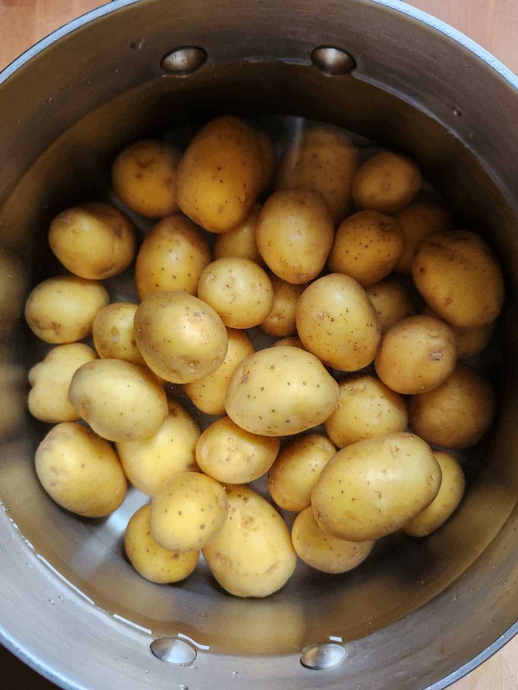 Whole potatoes in a pot filled with water.