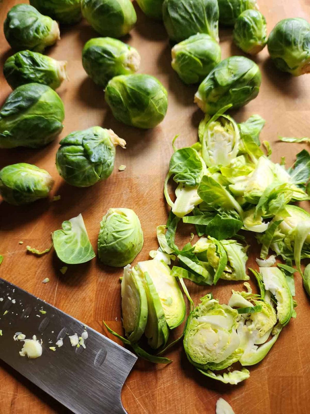 Brussel sprouts on a cutting board with a knife to the left.