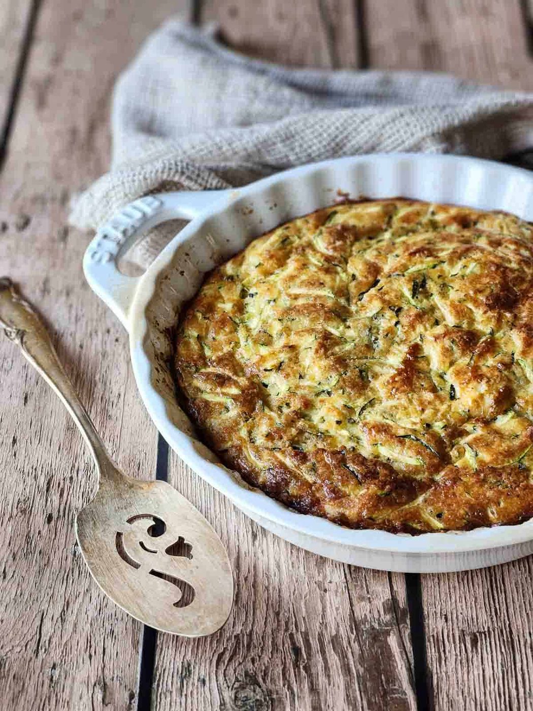 Zucchini pie in a white dish on a wood surface.