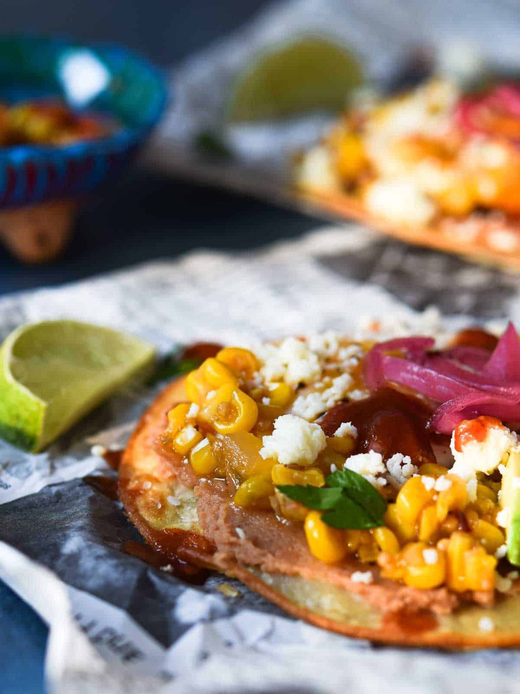 Close-up of a Mexican Huevos Rancheros tostada on newspaper with a lime next to it.