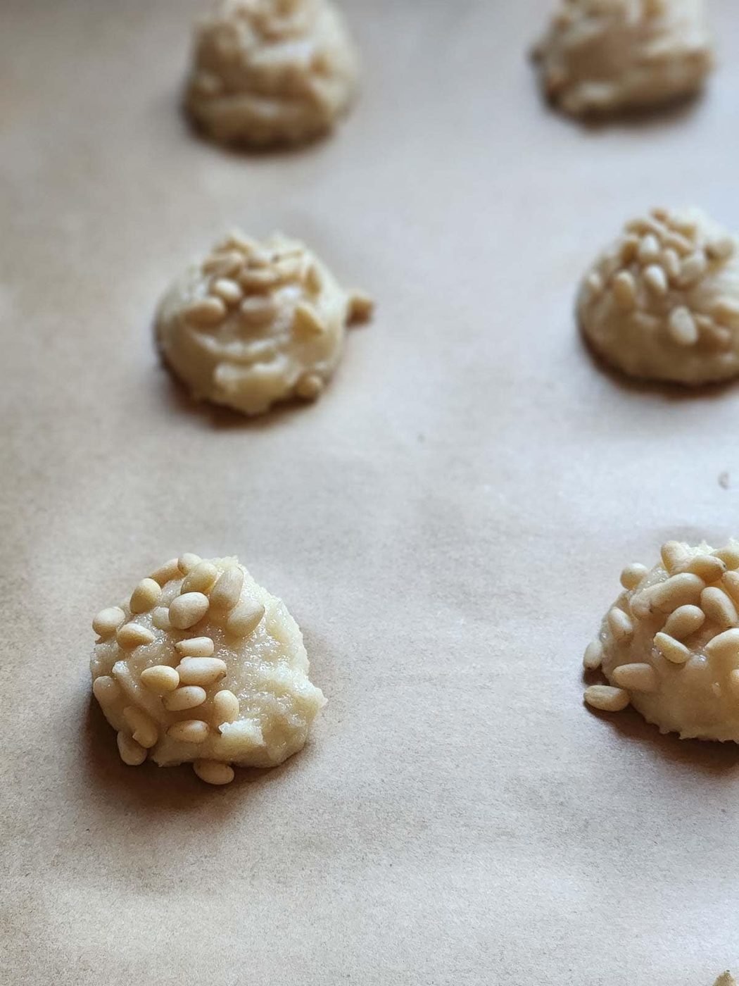 Scoops of cookie batter with pine nuts on parchment paper.