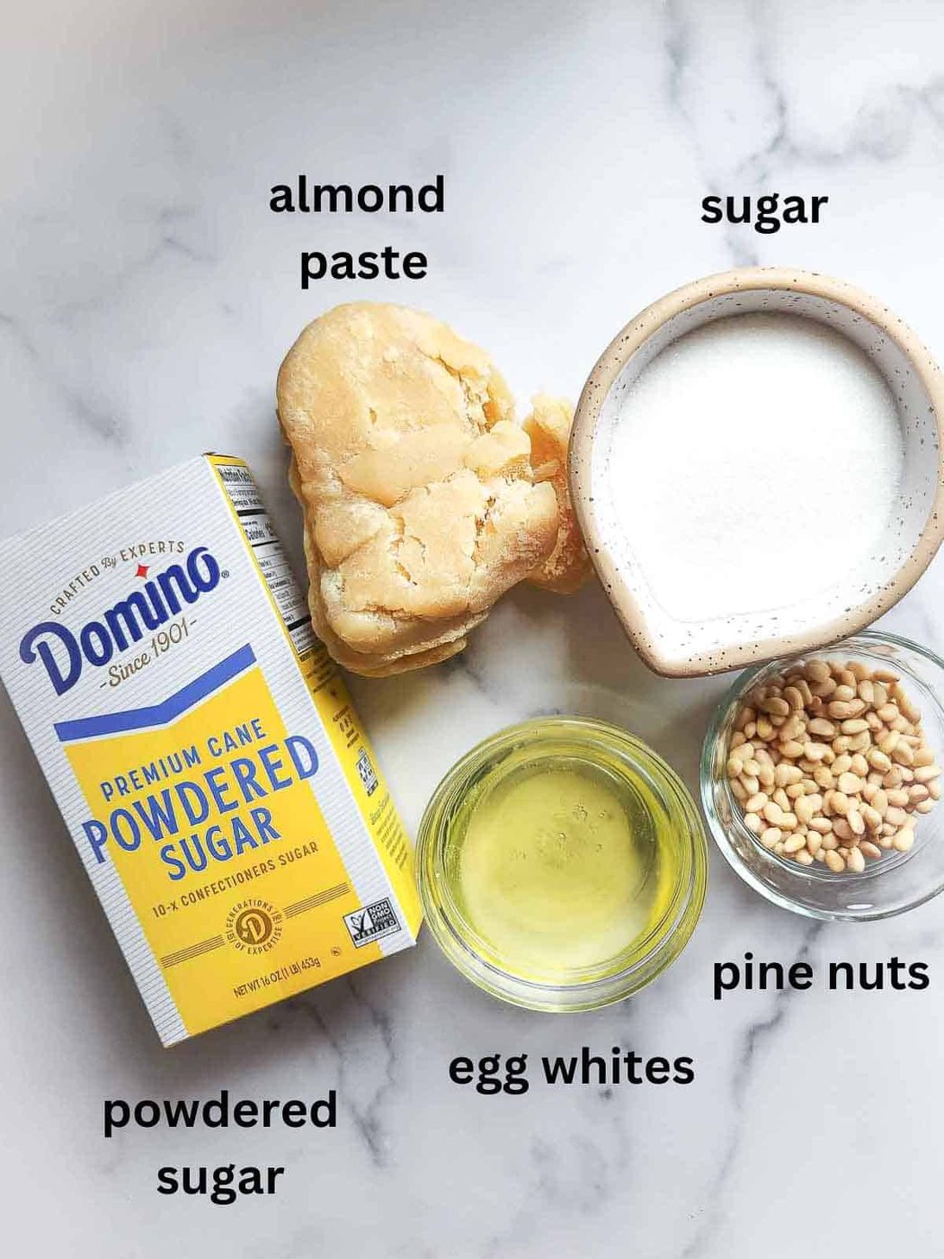 Ingredients for Italian pignoli cookies on a marble surface.