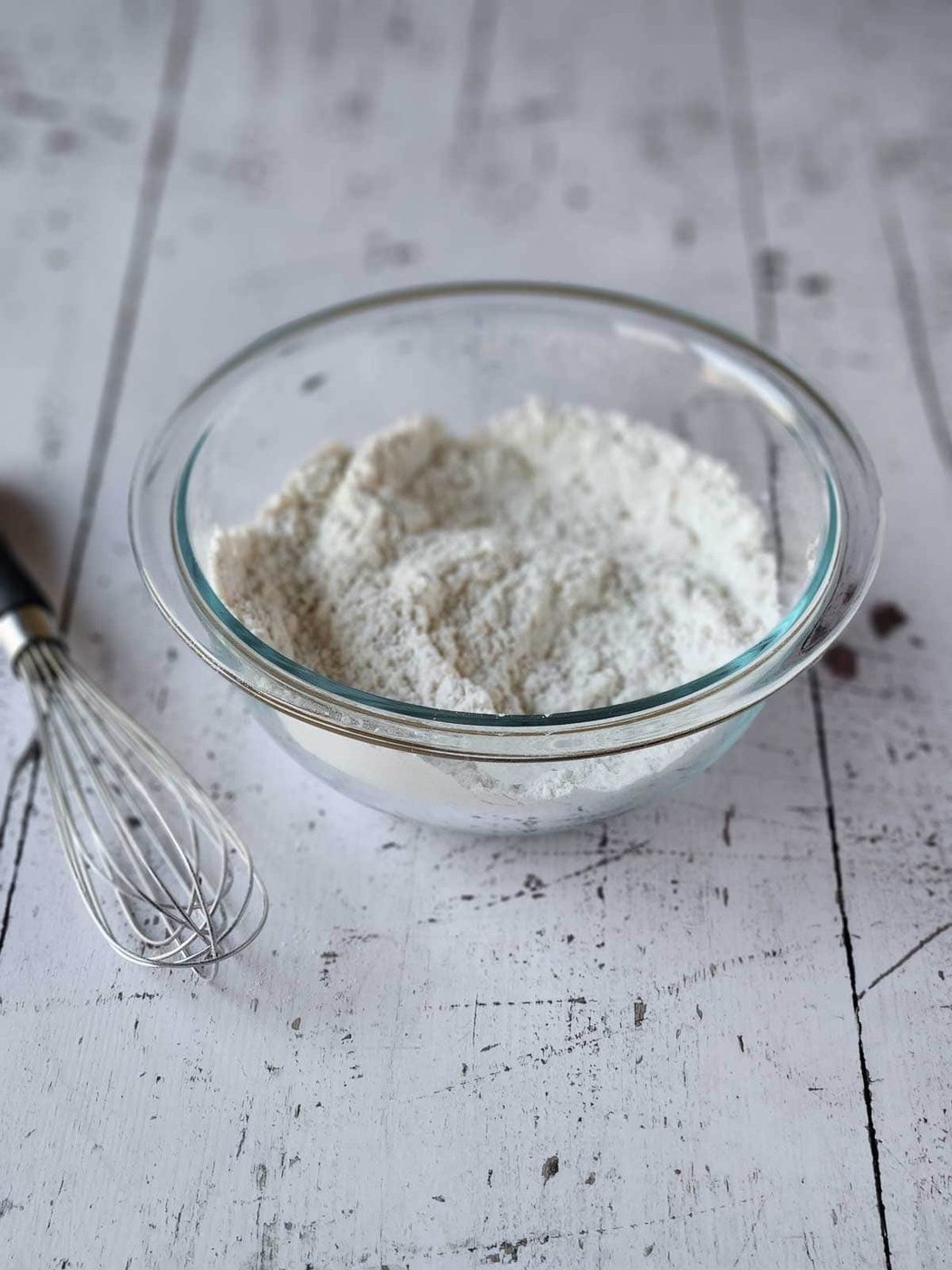 Flour mix in a clear bowl with a whisk next to it.