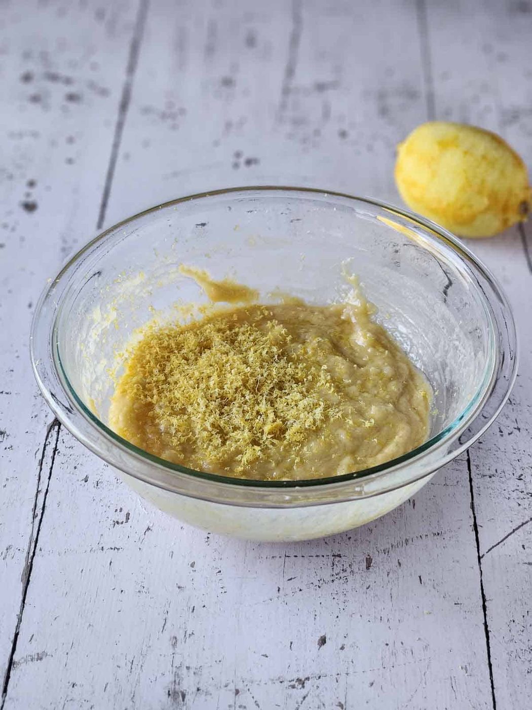Batter for lemon pizzelles with lemon zest on top in a clear bowl.