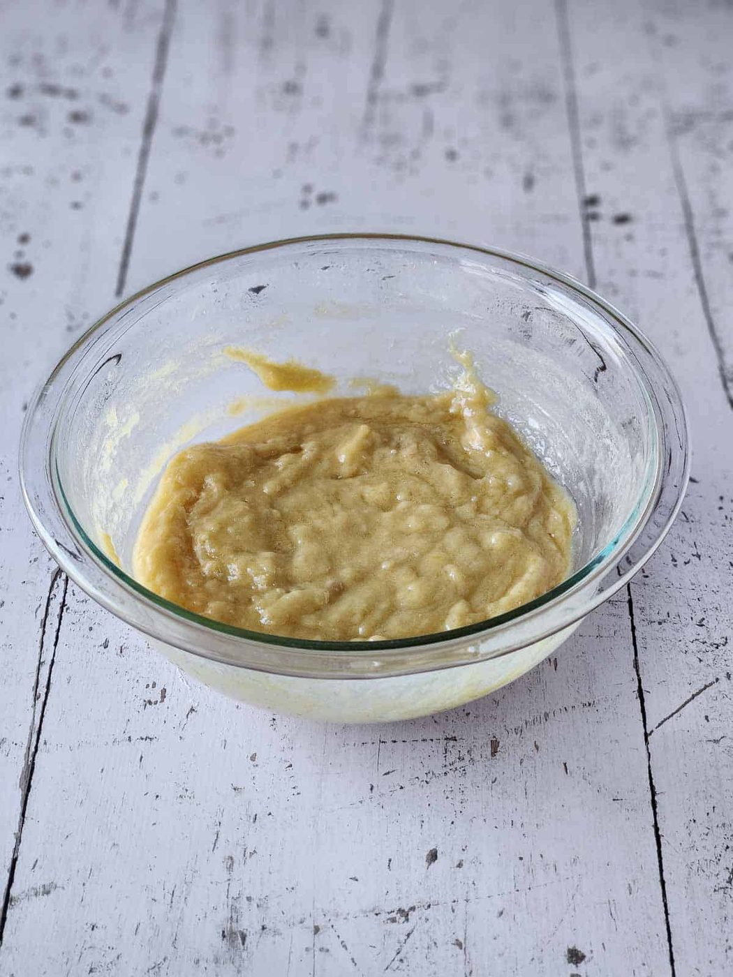 Batter for lemon pizzelles in a clear bowl on white wood.