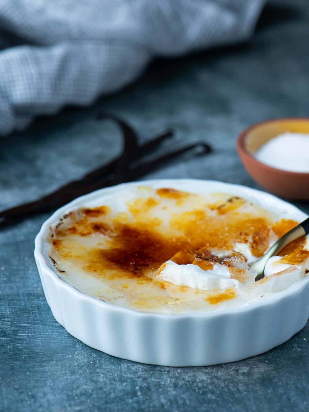 Vanilla yogurt brulee in a white ramekin with a spoon.