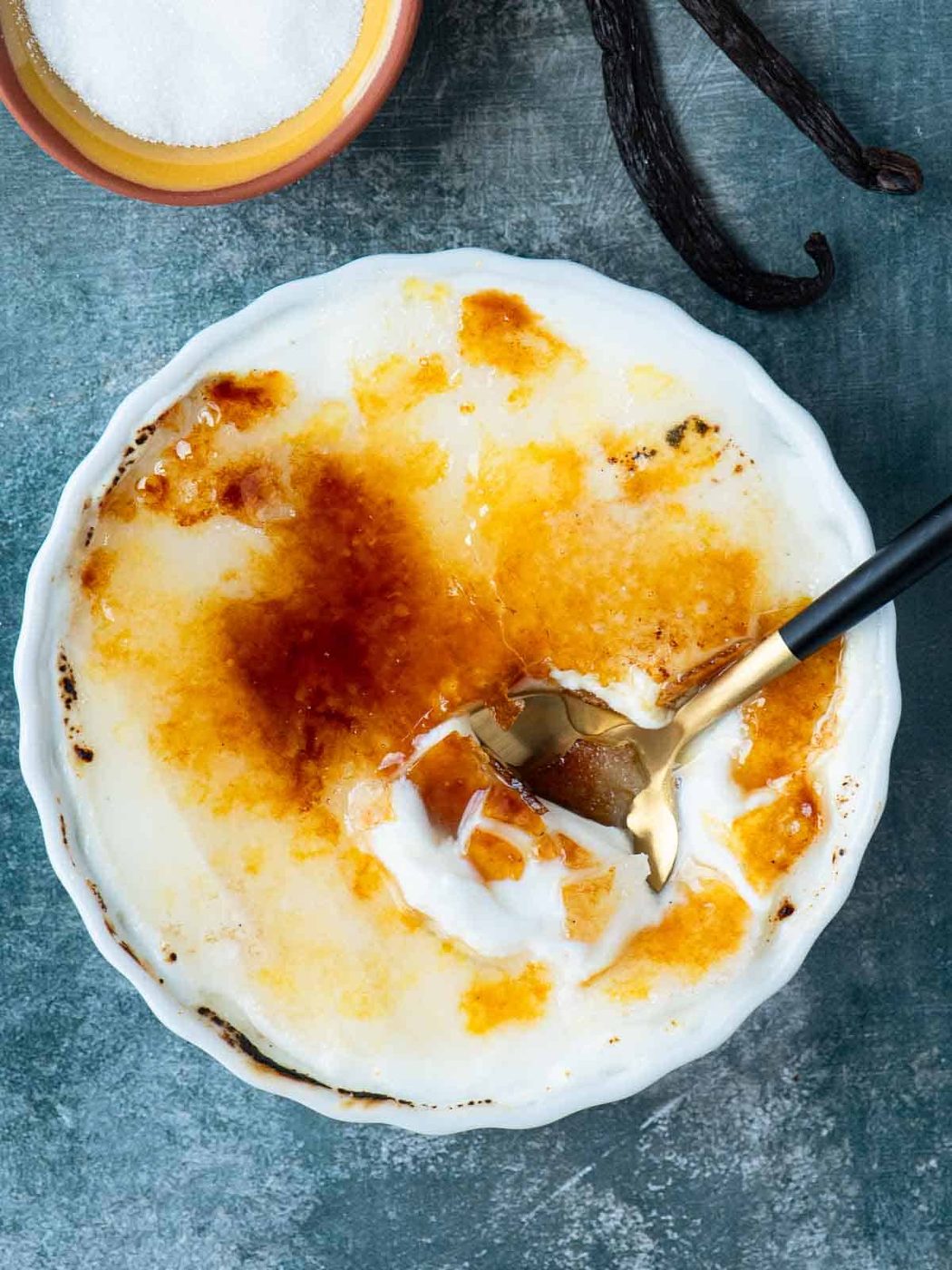 Overhead of creme brulee on a blue surface with a spoon in it.