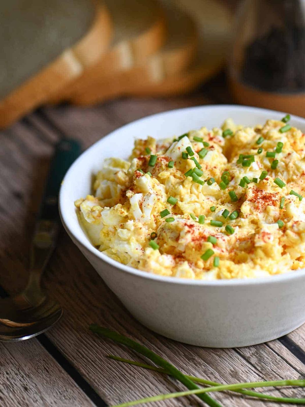 Egg salad in a white bowl with paprika and chives placed on a wooden table.