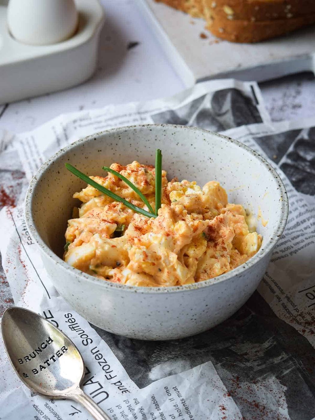 Close up of egg salad in a bowl with paprika and chives.