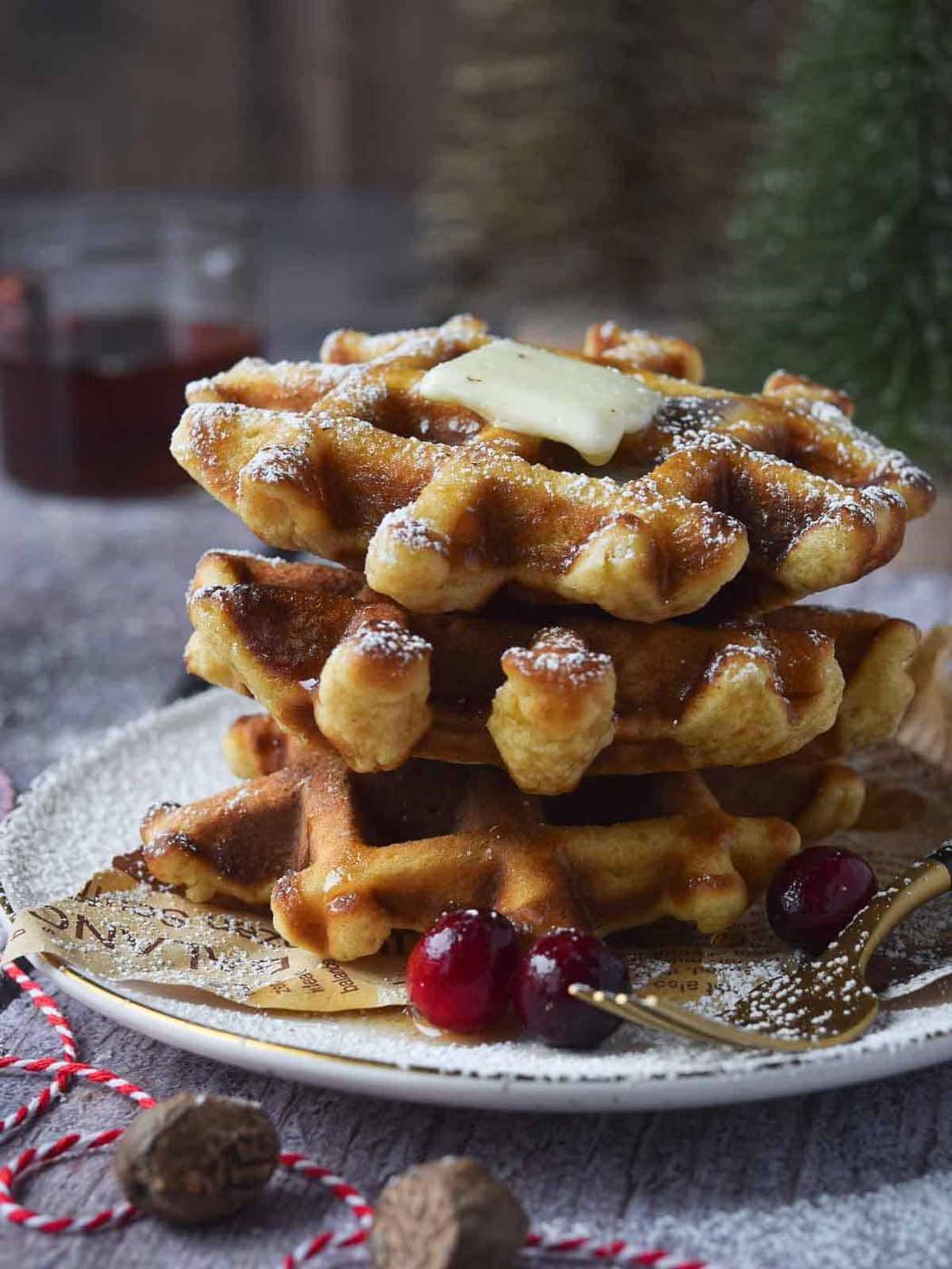 Eggnog waffles stacked on a plate with butter and powdered sugar.