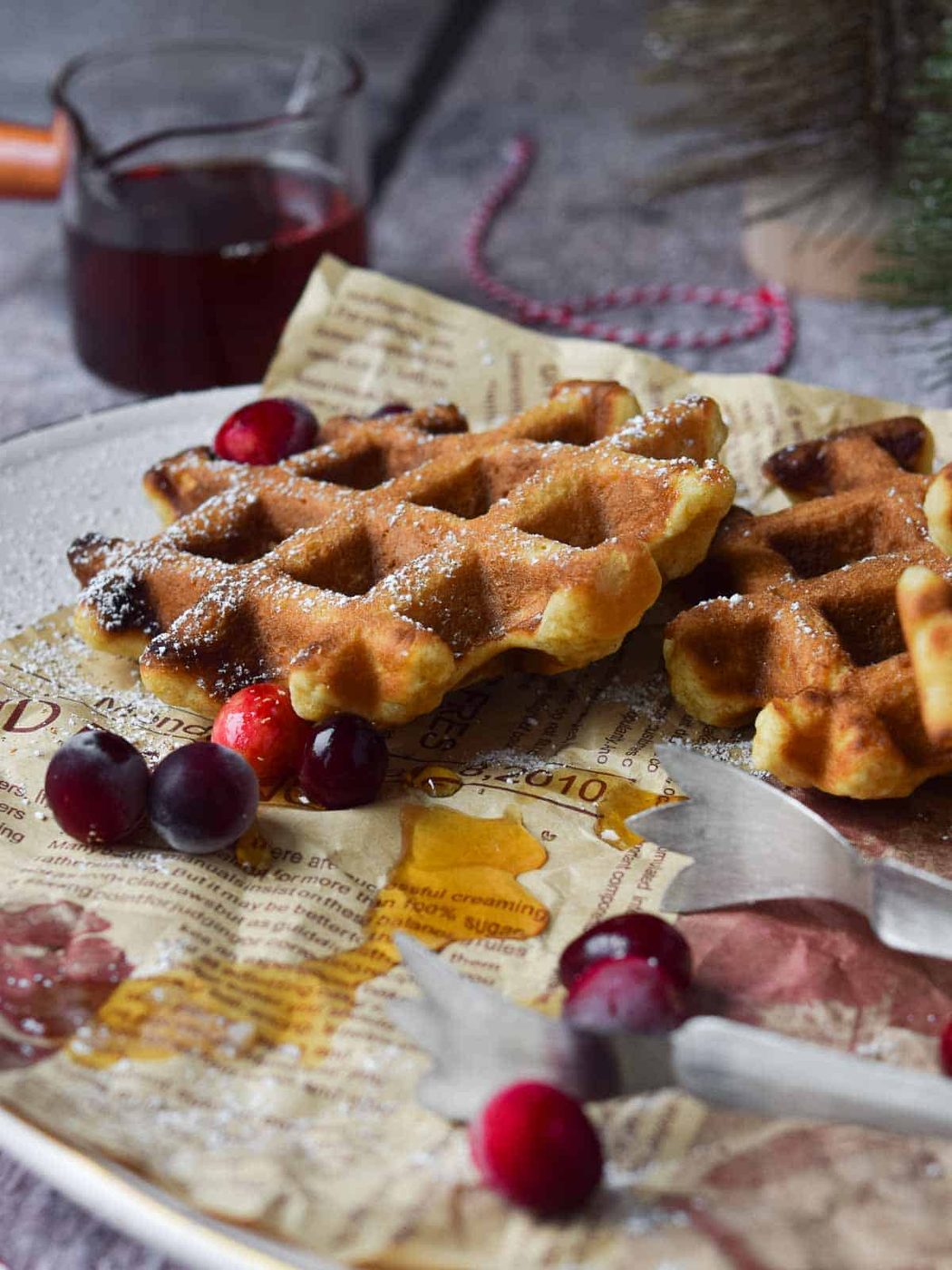 A platter of waffles with serving tongs and maple syrup.