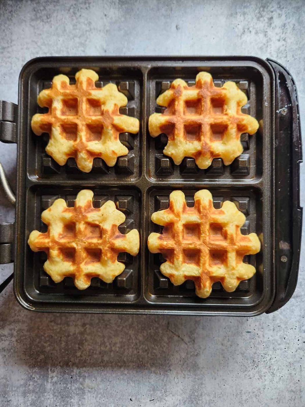 Four cooked waffles on a waffle maker.