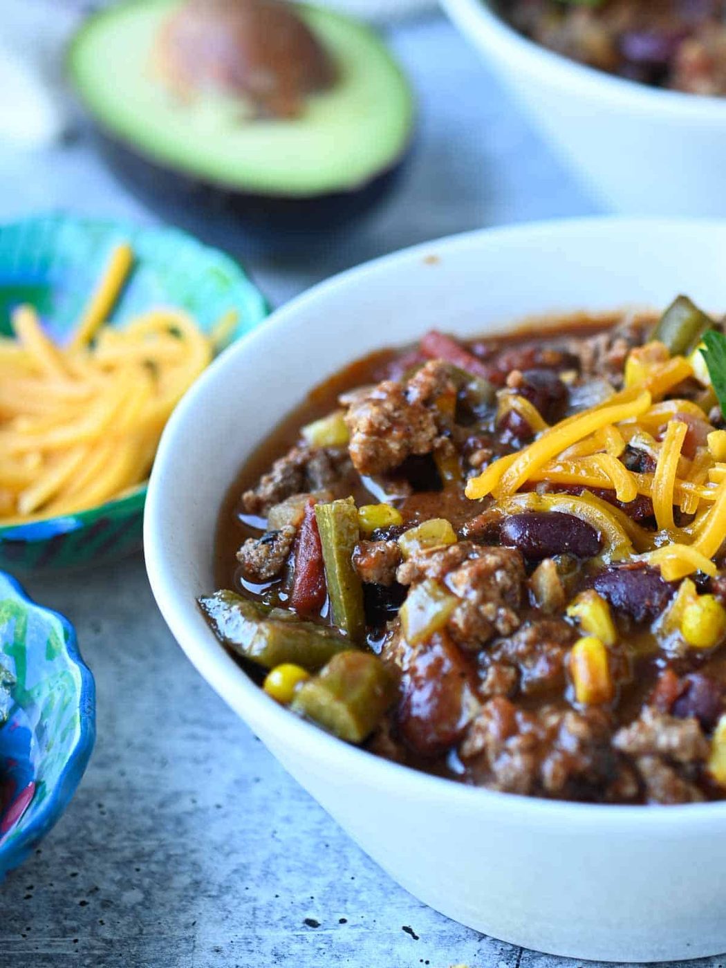 Close-up of chili in a white bowl, with an avocado in the back.