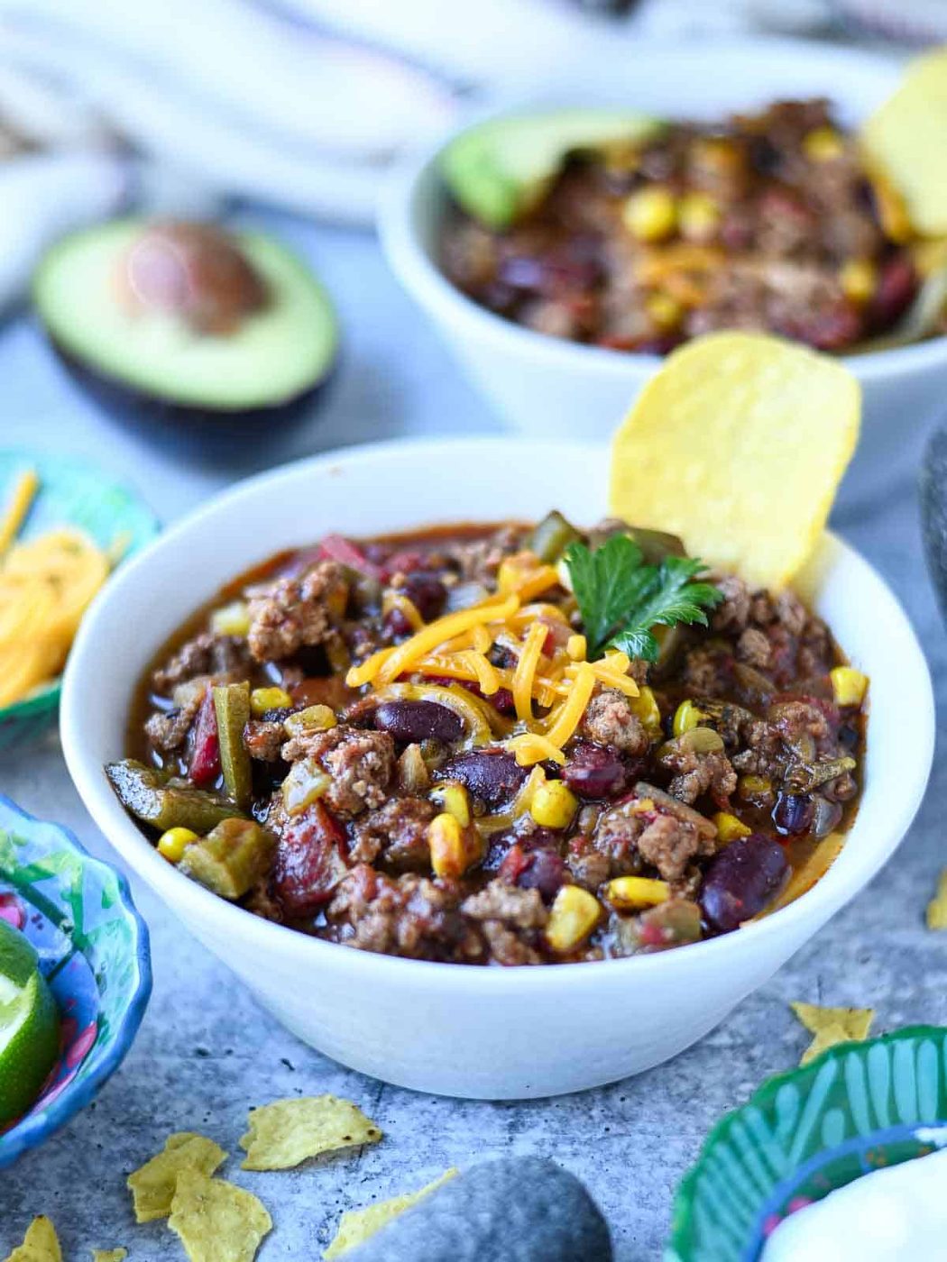 Two bowls of chili in a white bowl on a blue surface.