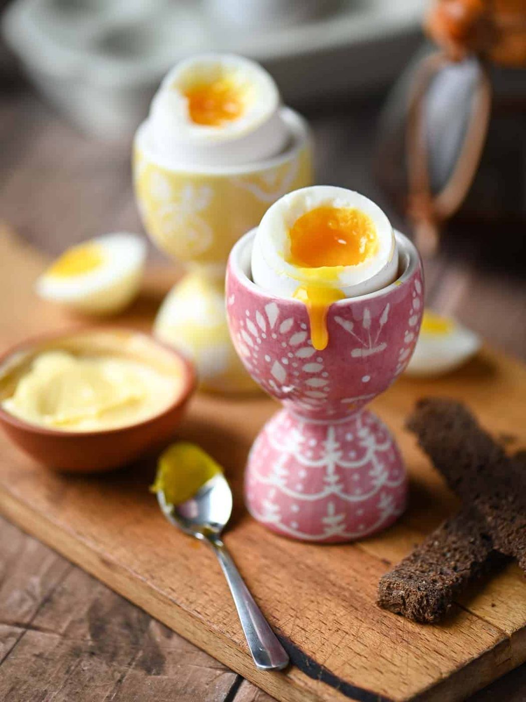 Two soft boiled eggs in egg holders with the yolk dripping down.