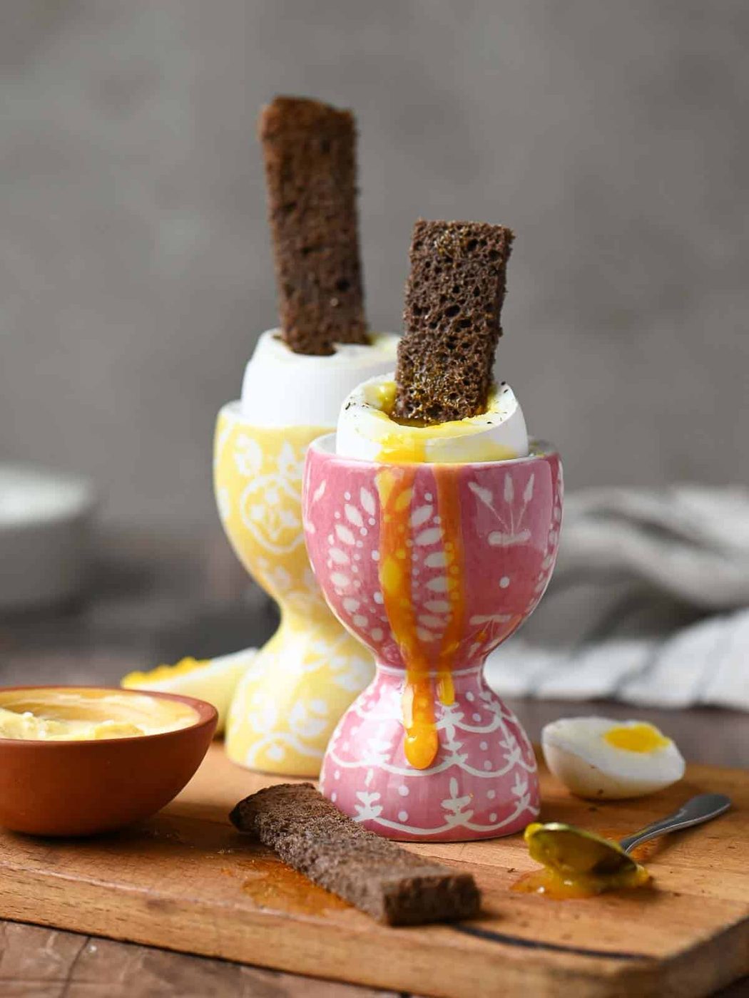 Eye level view of two soft boiled eggs in pink and yellow egg holders with toast.