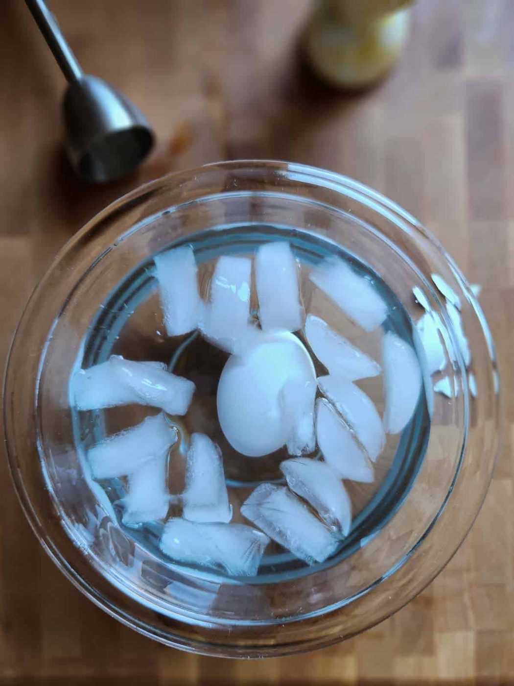 Overhead of an egg in a clear bowl with water and ice.