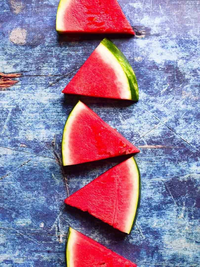 Overhead of sliced watermelon triangles on a blue surface.
