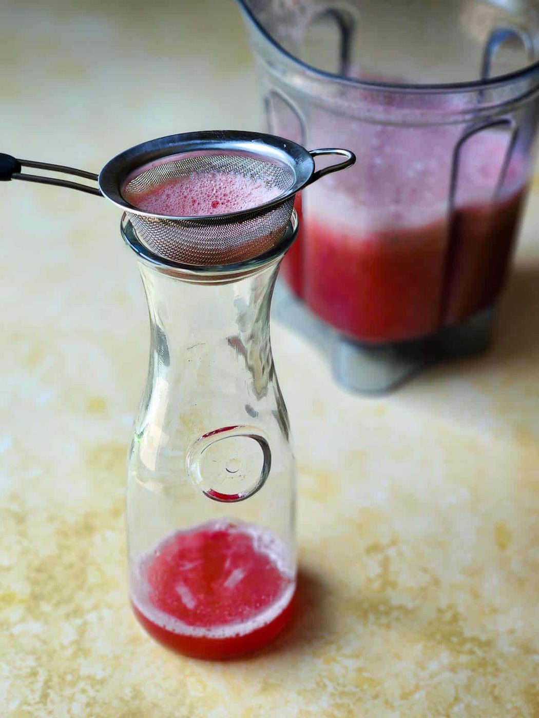 Watermelon juice in a pitcher with a strainer on top.