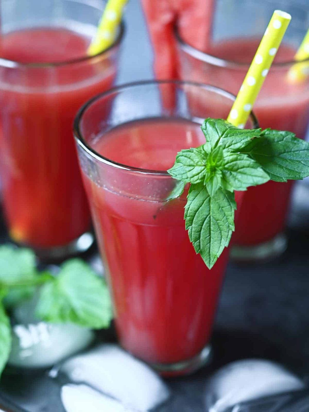 Close-up of watermelon water with mint in a clear glass with a yellow straw.