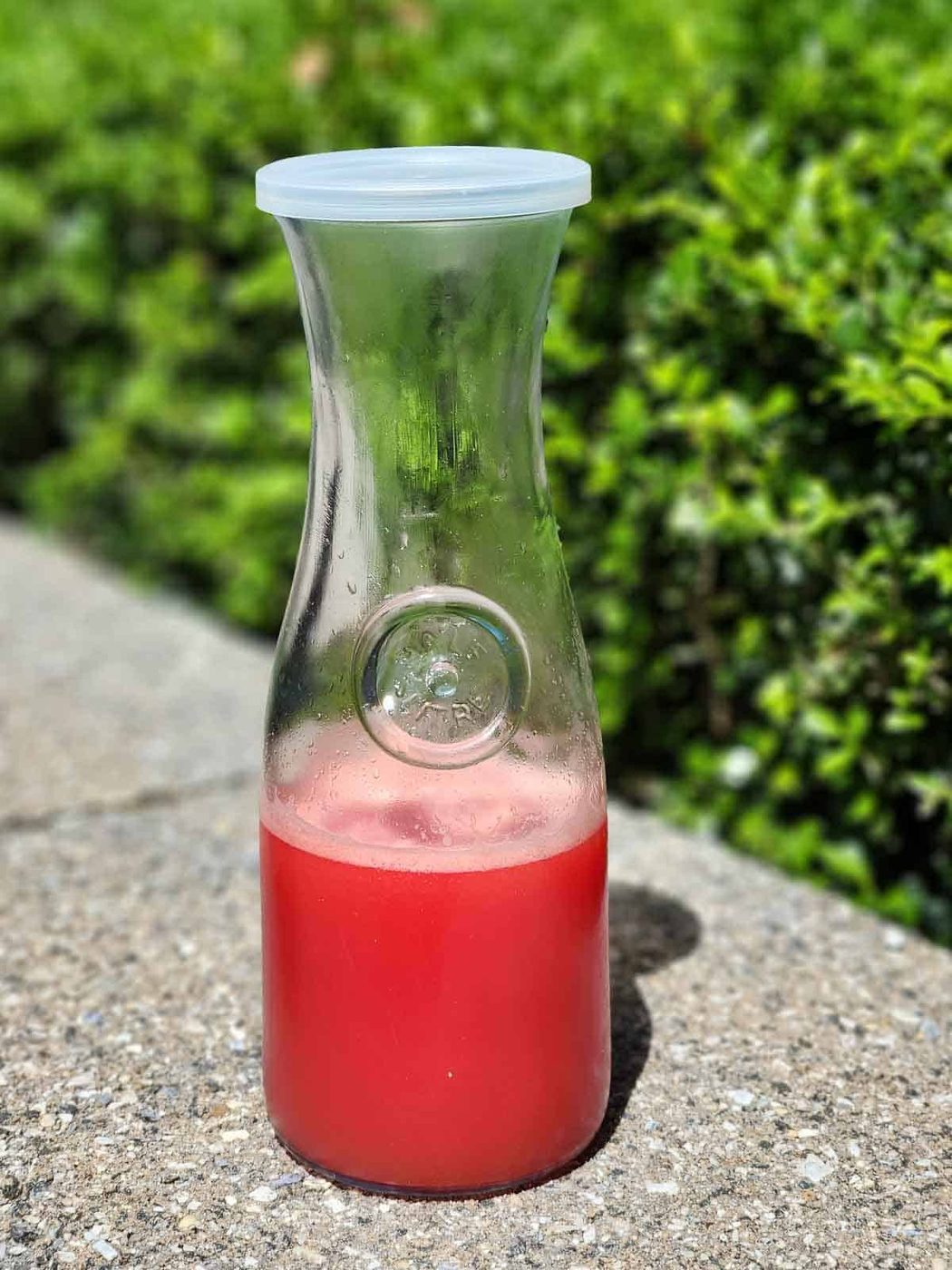 Watermelon water in a clear carafe outside.