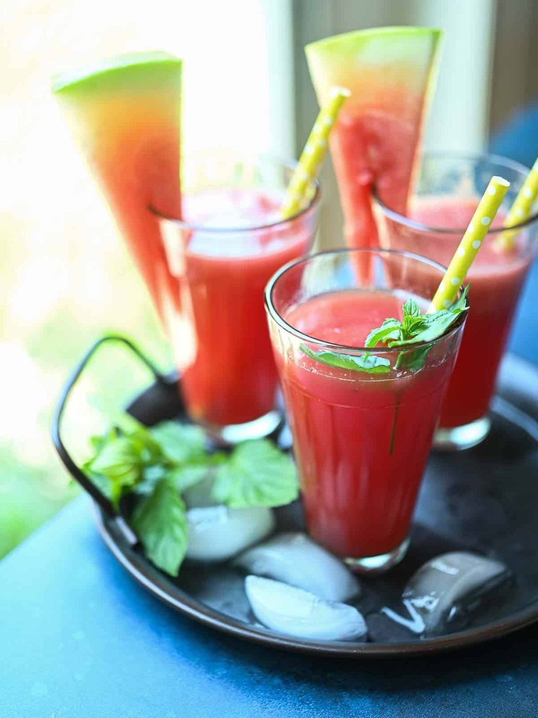 Three glasses on watermelon water on a tray by the window.