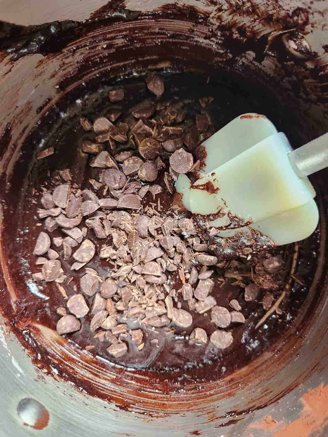 Folding chocolate chips into brownie batter with a spatula.