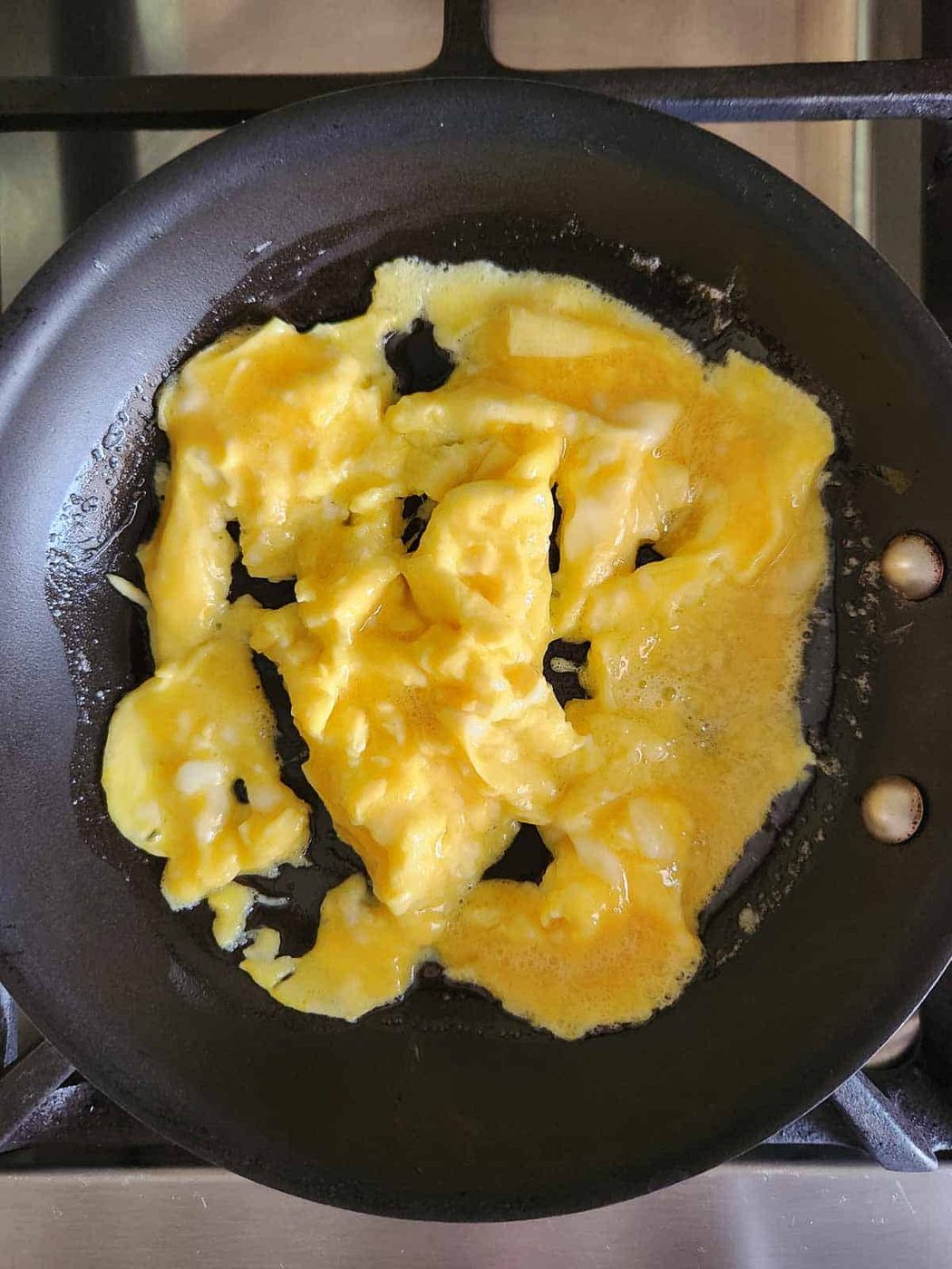 Semi-cooked scrambled eggs in a skillet.