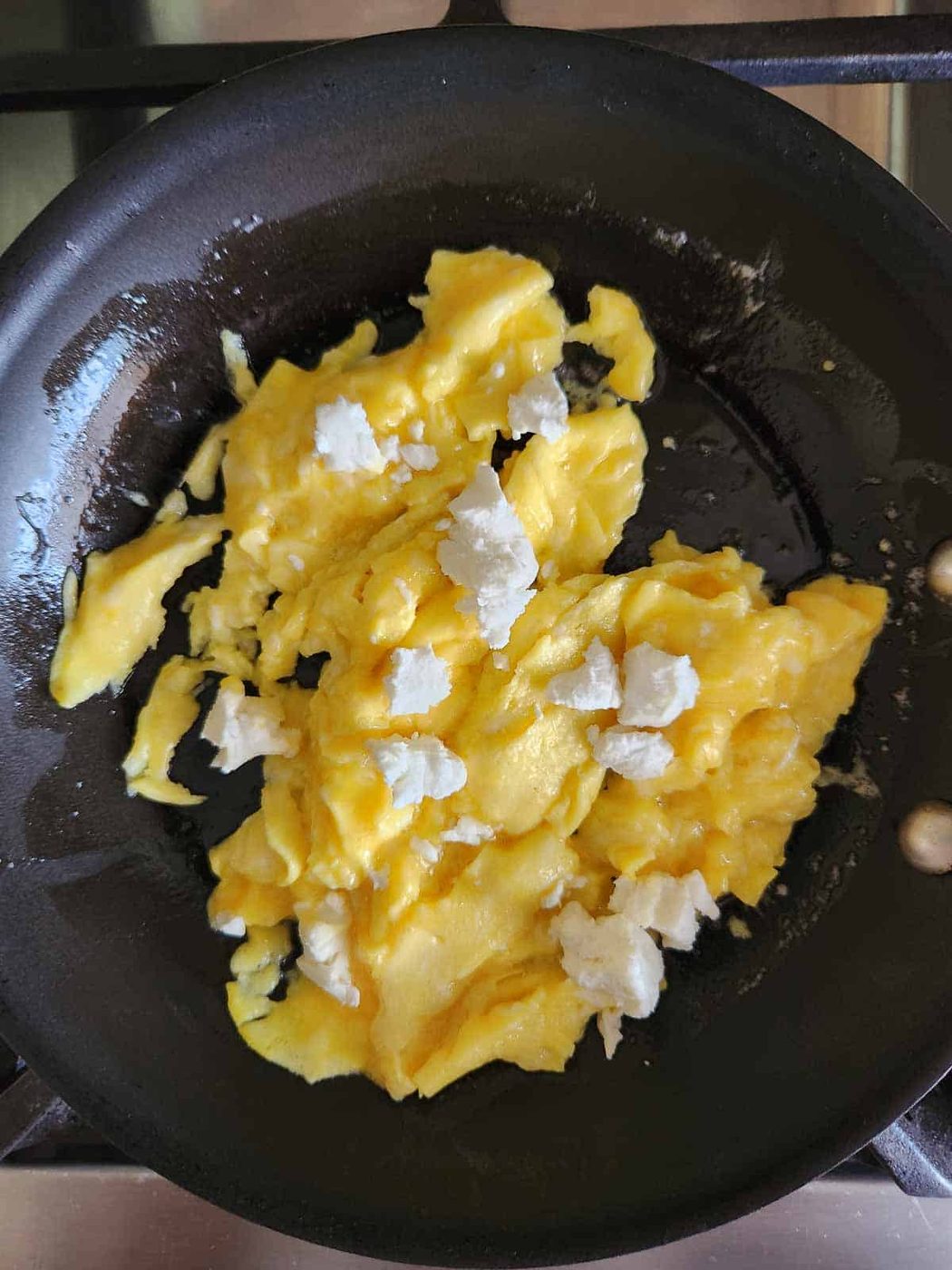 Scrambled eggs with goat cheese on top in a skillet.