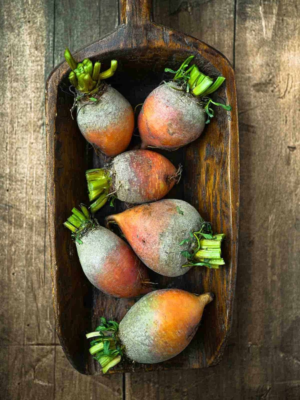 Overhead of raw golden beets on a wooden surface.